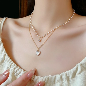 Détail d'un collier double épaisseur doré avec pendentif cœur et perles sur un mannequin