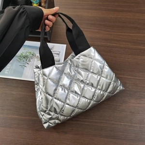 Gros plan d'un sac cabas argenté matelassé avec des poignées en tissu noir sur table