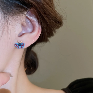 Close-up of blue butterfly stud earring with red rhinestones on a female model