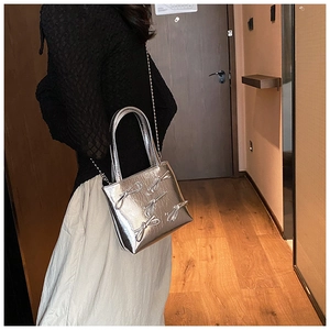 Silver square bag with bow details and metal chain strap shown worn by a model
