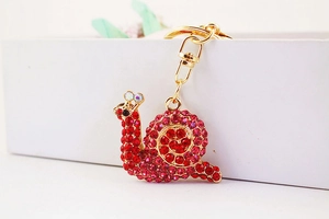 Close-up of golden snail keychain with red rhinestones hanging on a white gift box
