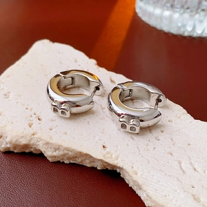 Detail of silver hoop earrings with B-letter charm on a natural stone surface