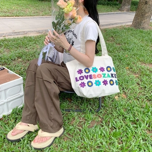 Detailed shot of white canvas tote bag with colorful daisy embroidery and sturdy handles
