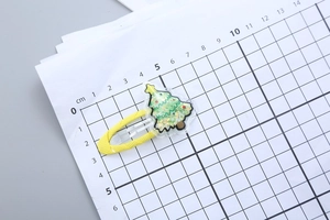 Macro view of Christmas tree hair clip with quicksand glitter on a size scale ruler