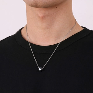 Gros plan d'un collier en acier titane argenté avec un pendentif cube noir et lettre N