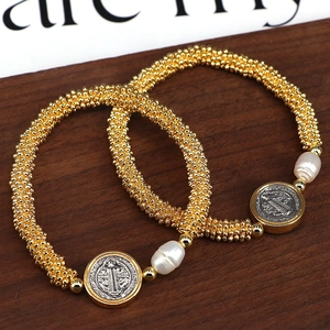Vintage gold beaded bracelet with a baroque pearl and religious coin pendant on wood