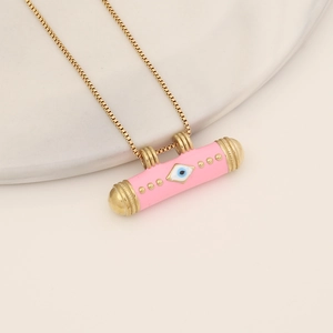 Close-up of pink enamel cylindrical evil eye pendant with golden chain on beige tray