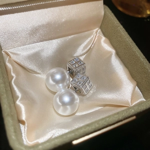 Macro detail of silver pearl earrings with cubic zirconias in a beige silk gift box