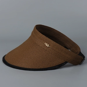 Detail of sun visor with straw weave texture and golden leaf emblem on a dark grey background