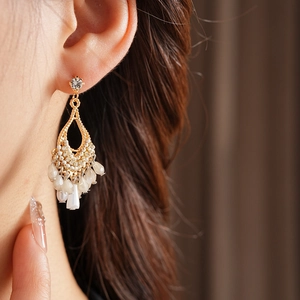 Detail of gold teardrop tassel earrings with white beads and rhinestone on a model