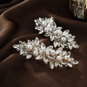 Close-up of hair clips featuring marquise crystals and pearls on a brown silk background