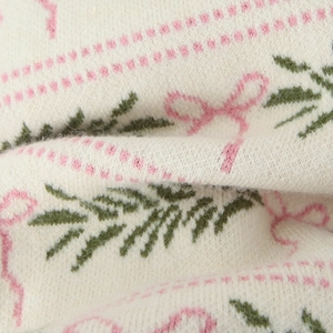 Close-up of knit sweater fabric with pink bow jacquard pattern on off-white base