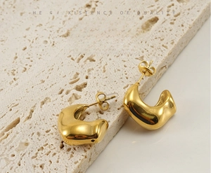 Détails de boucles d'oreilles dorées de forme organique sur pierre de travertin beige