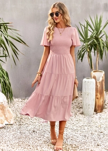 Pink tiered midi dress with smocked bodice and flutter sleeves in an outdoor garden