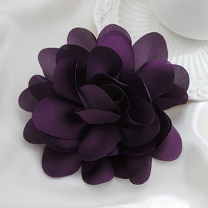 Macro detail of dark purple fabric flower brooch with layered petals on white silk