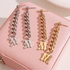 Boucles d'oreilles pendantes lettre M en or et argent sur une boîte à bijoux