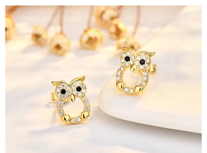 Macro view of gold owl stud earrings with sparkling zircon stones and black gemstone eyes