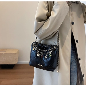 Detail of black quilted shoulder bag featuring gold heart charms and chain straps