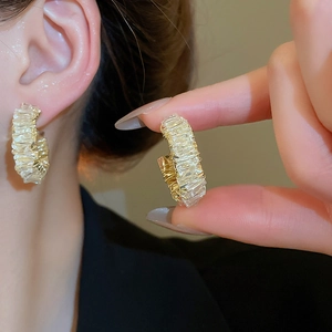 Detailed view of C-shaped gold-wrapped earrings with crystals shown on an ear and hand