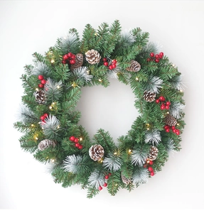 Detail of snowy Christmas wreath with red berries, pine cones and warm LED lights