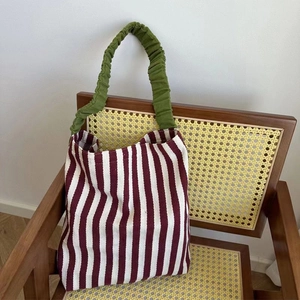 Detail of striped knit tote bag with green ruffled handle on a vintage rattan chair
