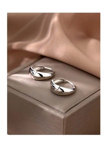 Polished silver metal hoop earrings displayed on a luxury silk fabric background