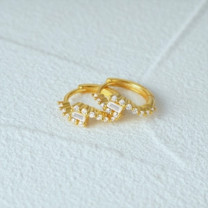 Macro detail of S925 silver hoop earrings with rectangular and round white zircons