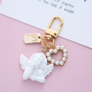 Detail of a vintage golden keychain with baroque angel, pearl heart, and engraved metal tag