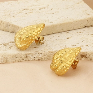 Close-up of gold-plated textured heart earrings on a stone surface with soft lighting