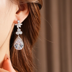 Close-up of elegant silver floral earrings with pear-shaped zircon drops on a model