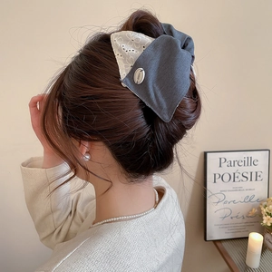 Détail d'une pince à cheveux à nœud en dentelle grise et blanche portée par un mannequin