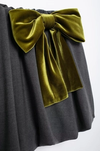 Détail d'un grand nœud en velours vert olive sur la taille d'une jupe grise foncée