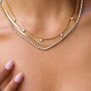 Détail d'un collier triple épaisseur doré avec zircon carré et chaîne serpent élégante