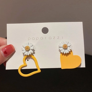 Detail view of asymmetric daisy heart earrings featuring yellow heart charms and white petals