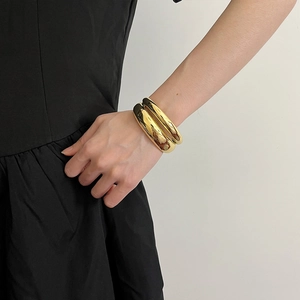 Close-up of wide polished gold double-layered open cuff bracelets on model's wrist
