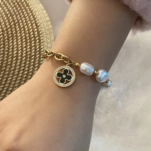 Detailed close-up of a gold chain bracelet with white pearls and a black clover charm