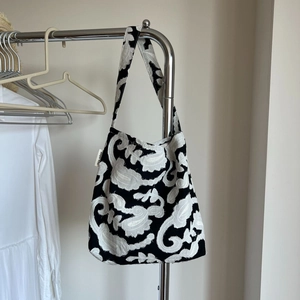 Minimalist black and white paisley embroidered cotton linen tote bag on a hanger