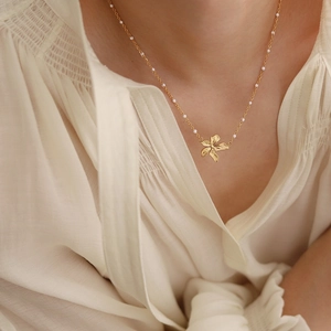 Detail of 18K gold-plated floral pendant necklace with white beads on model collarbone