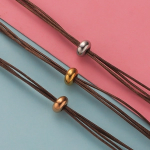 Macro shot of silver, gold, and rose gold stainless steel beads on dark brown cord bracelet
