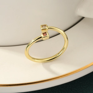 Elegant gold open ring featuring square white and orange-red gemstones on a ceramic dish