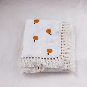 Close-up of white cotton muslin baby blanket with orange fruit print and cream tassels