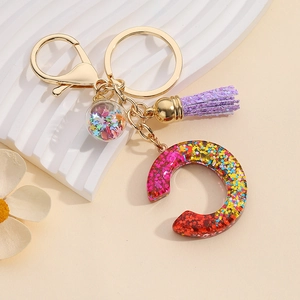 Detail of letter C resin keychain with colorful glitter, purple tassel and gold hardware