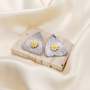 Close-up of triangle stud earrings with daisy flower enamel on a beige stone surface