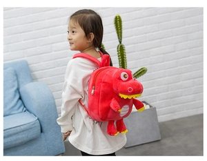 Side view of a toddler wearing a red plush dinosaur backpack in a living room