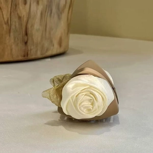 Detail shot of a cream fabric camellia flower hair claw clip on a brown base
