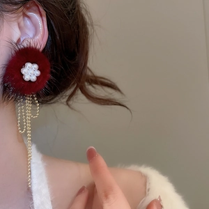 Detail of red fur flower earrings with white pearls and gold tassel chains on model