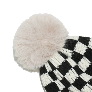 Close-up of black and white checkered knit hat featuring a soft beige faux fur pompom top