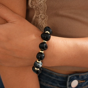 Detail of beaded bracelet with oversized black acrylic beads and gold spacers on wrist