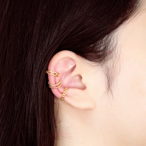 Dettaglio di un set di ear cuff dorati infinity e testurizzati sulla cartilagine dell'orecchio
