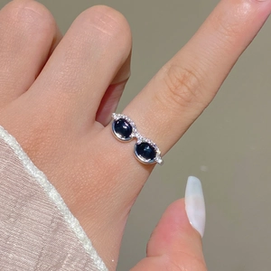 Close-up of creative silver sunglasses ring with black stones worn on person's index finger